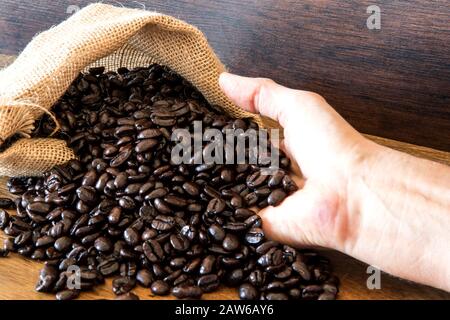 Hands hold Coffee Beans in bag on wooden background. Stock Photo