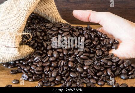 Hands hold Coffee Beans in bag on wooden background. Stock Photo