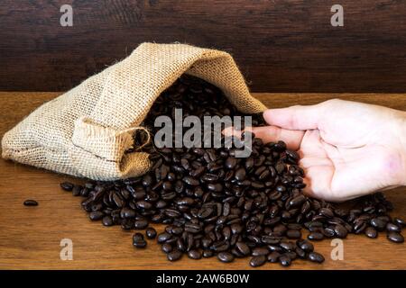Hands hold Coffee Beans in bag on wooden background. Stock Photo