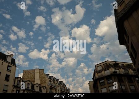 Late afternoon, summer in Paris, France, fluffy white clouds floating over attic windowed Paris Apartment buildings on a sunny blue sky day Stock Photo