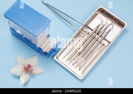 Set of composite filling instruments for dental treatment and plastic box with cotton tampons on blue background. Medical tools in stainless steel tra Stock Photo