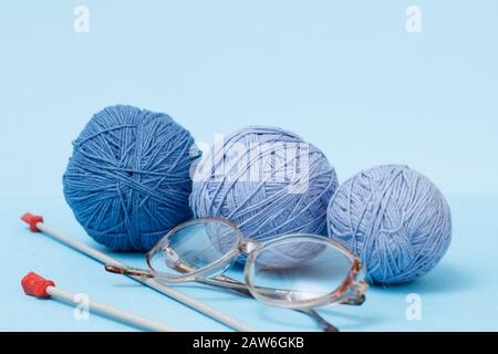 Knitting yarn balls, metal knitting needles and glasses on a blue background. Knitting concept. Stock Photo