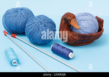 Knitting yarn balls, metal knitting needles, threads and wicker basket on a blue background. Knitting concept. Stock Photo