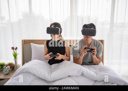 Asian couple lover Enjoying Playing Videogame at bed room, Asia couple lover  feeling happy fun and virtual reality, VR playing games together while l Stock Photo