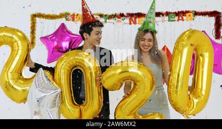 Asian couple lover holding 2020 numbers celebrating a new year at a bar shouting and laughing and Counting down to midnight on a new year party Stock Photo