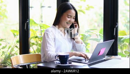 Asian Business women are using mobile and touch smart phone for Communication and women using notebook for working in coffee shop Stock Photo