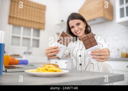 Dark-haired woman in a striped blouse holding two bars of chocolate Stock Photo