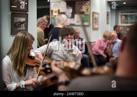 Local residents playing during a music session at the Colonsay Hotel on the the Inner Hebridean island of Colonsay on Scotland's west coast.  The island is in the council area of Argyll and Bute and has an area of 4,074 hectares (15.7 sq mi). Aligned on a south-west to north-east axis, it measures 8 miles (13 km) in length and reaches 3 miles (4.8 km) at its widest point, in 2019 it had a permanent population of 136 adults and children. Stock Photo