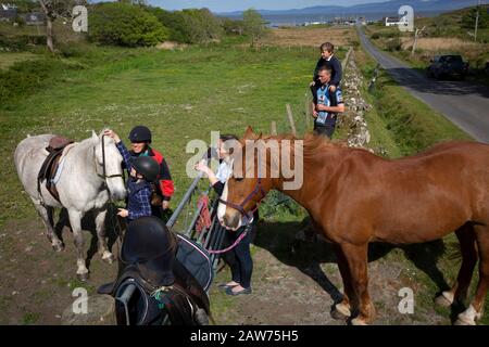 Local GP Jan Brooks (second left) giving a riding lesson to an islander on the the Inner Hebridean island of Colonsay on Scotland's west coast.  The island is in the council area of Argyll and Bute and has an area of 4,074 hectares (15.7 sq mi). Aligned on a south-west to north-east axis, it measures 8 miles (13 km) in length and reaches 3 miles (4.8 km) at its widest point, in 2019 it had a permanent population of 136 adults and children. Stock Photo