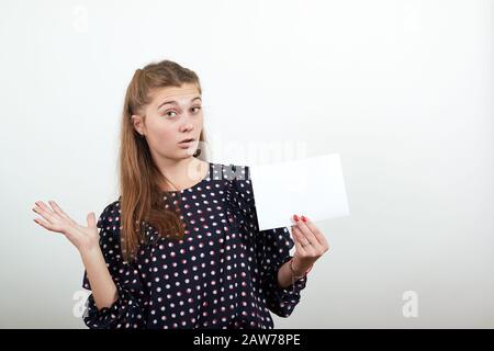 Fair-haired girl in black dress with white circles shows blank paper in surprise Stock Photo