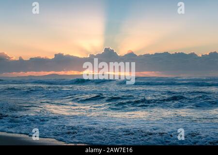 Spectacular sunrise seascape of ocean waves and sun beaming through the clouds. Stock Photo