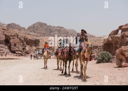 PETRA, JORDAN - MAY 18, 2018: Crowd of tourists riding camels visiting the archeological site of Petra, part of Unesco Heritage Stock Photo