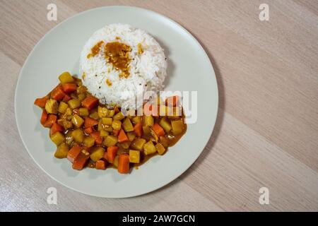 Cooked rice, curry with chicken, carrot and potato close-up on a plate on a table. Horizontal top view from above. Stock Photo