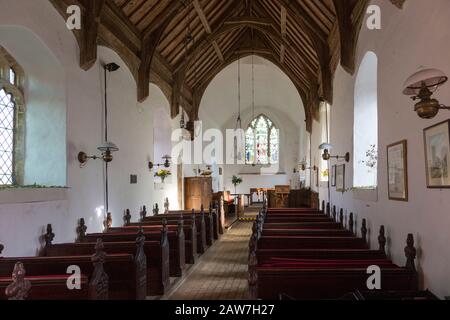Looking east down the nave towards the altar and east window with historic wooden carved pews, fine wooden roof, whitewashed walls, interior of small Stock Photo