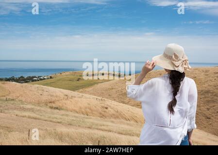 Woman in sunhat and white shirt looking at rolling hills and ocean landscape of South Australia Stock Photo