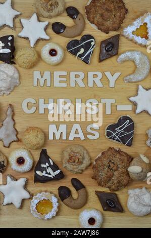 different kinds of Christmas cookies on a breadboard around the words: MERRY CHRISTMAS Stock Photo