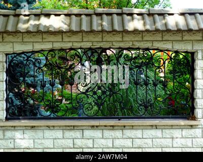 black wrought iron fence with frame. ornate decorative steel design in textured concrete wall structure. colorful lush foliage. mediterranean garden. Stock Photo