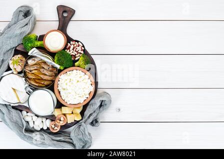 Food with calcium. A variety of foods rich in calcium: cheese, milk, parmesan, sour cream, fish, almonds, parsley, garlic, broccoli. On a white wooden Stock Photo