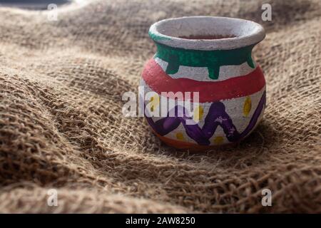 Handcrafted earthen pot over a sack bag. Clay vase made out of mud on cloth background. Stock Photo