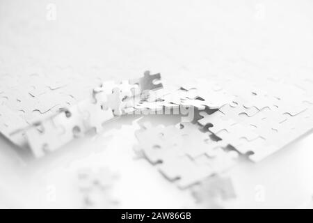 On a white table is a white puzzle, disassembled or broken into pieces on one side. Stock Photo