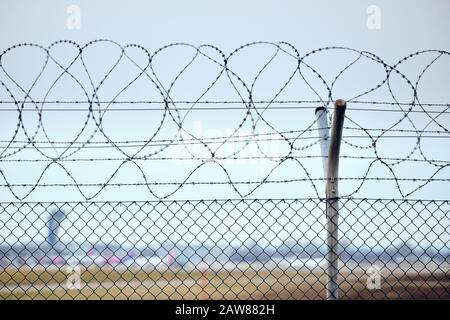 High chain-link fence with razor-barbed wire at the top protecting an airport. Stock Photo