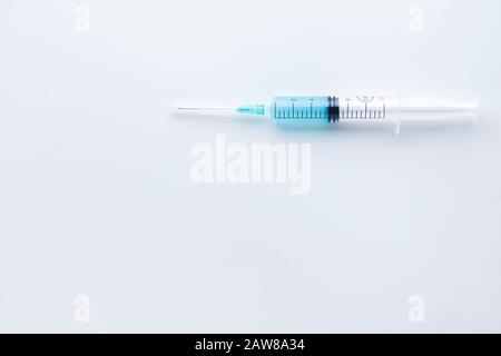 Single syringe filled with light blue liquid placed horizontally on white background Stock Photo