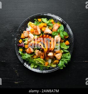 Pumpkin salad with chicken meat and vegetables in a black plate on a black background. Top view. Free space for your text. Stock Photo