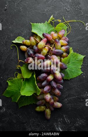 Fresh red grapes with leaves on a black stone table. Top view. Free space for your text. Stock Photo