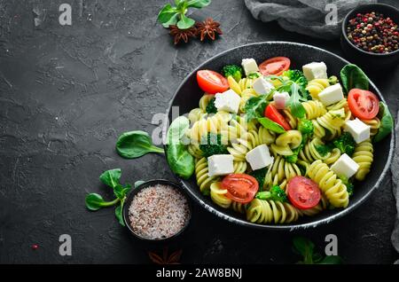Pasta with spinach, tomatoes and feta cheese. In a black plate on a wooden background Top view. Free space for your text. Flat lay Stock Photo