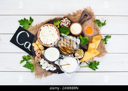 Food with calcium. A variety of foods rich in calcium: cheese, milk, parmesan, sour cream, fish, almonds, parsley, garlic, broccoli. On a white wooden Stock Photo