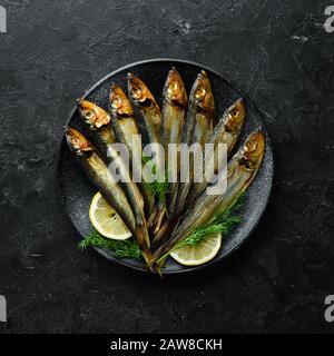 Smoked capelin fish with lemon on a black plate. Top view. Free copy space. Stock Photo