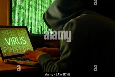 Hooded Hacker using a computer for working out an virus Stock Photo