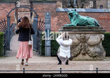 Hvilende loever, One of Two Resting Lions. Bronze sculptures in the King’s Garden at Rosenborg Castle, Copenhagen, Denmark. Women tourist taking photo