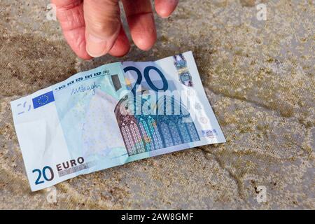 A lucky senior elderly person pensioner finds money on the ground hand reaches down to pick up a twenty Euros Euro note off the floor. Europe Stock Photo