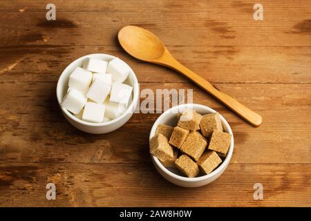 White and brown sugar cubes in white ceramic bowls on a wooden table Stock Photo