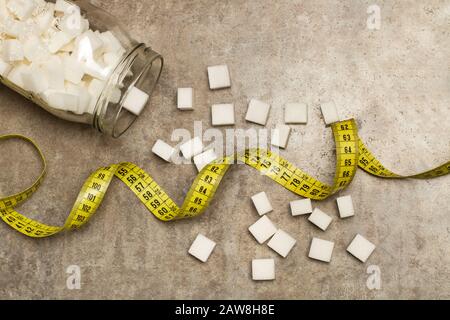 White sugar cubes in a crystal jar and on a marble table with a yellow measure tape Stock Photo
