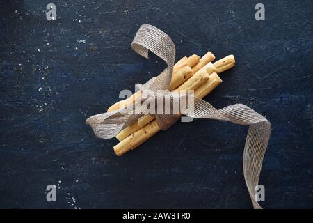 Closeup of grissini breadsticks tied together with a ribbon on dark background, breadsticks top view, italian breadsticks. Homemade, baked, soup Stock Photo
