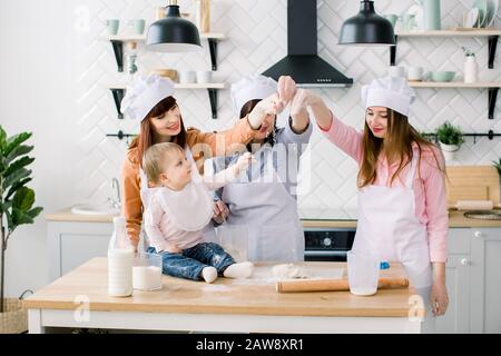 Three generations of women in white aprons are making pizza dough in the kitchen to Mothers Day. Stock Photo