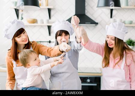 Three generations of women in white aprons are making pizza dough in the kitchen to Mothers Day. Stock Photo