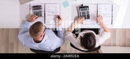Two Businesspeople Calculating Invoices With Calculators In Office Stock Photo
