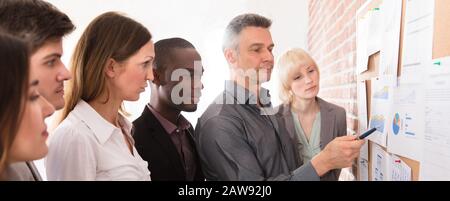 Manager Analyzing The Graph With His Co-workers Attached On Bulletin Board Stock Photo