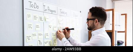 Businessman Writing On Sticky Notes Attached To White Board In Office Stock Photo
