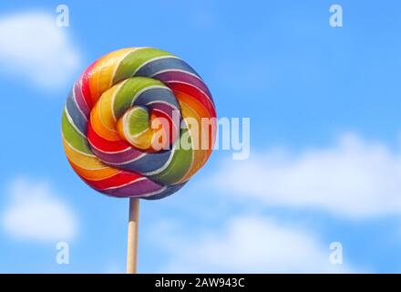 lollipop with rainbow colors in front of blue and white sky, cheerful background with copy space Stock Photo
