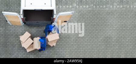 High Angle View Of Two Delivery Men Unloading Cardboard Box From Truck Stock Photo