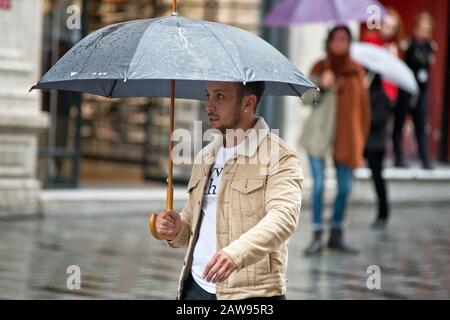 Istanbul: a young man walking under the rain with an umbrella in Istiklal avenue. Turkey Stock Photo