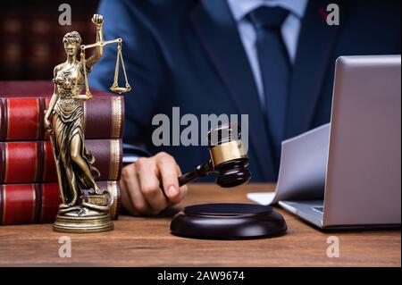 Midsection Of Judge Striking Gavel Near Mallet And Laptop At Desk In Courtroom Stock Photo