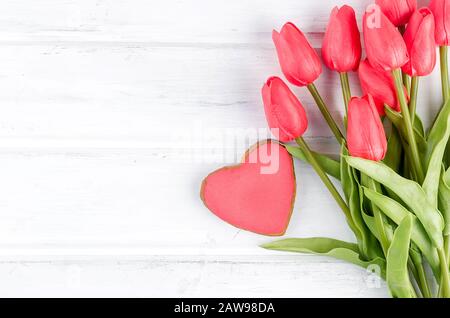 red gingerbread heart and a bouquet of tulips lying on white wooden background. Valentines Day or Mom Day concept. Copy space, flat lay, Template mock Stock Photo