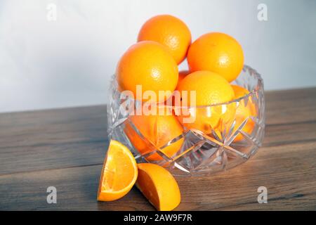 Lead crystal fruit bowl full of oranges 'fruit' against white background with cut orange wedges Stock Photo