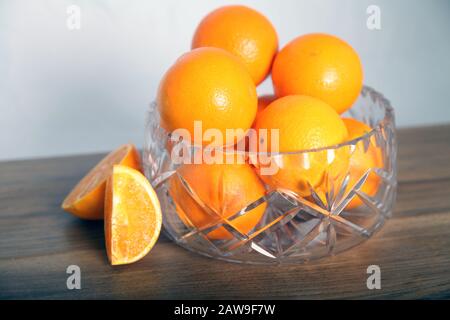 Lead crystal fruit bowl full of oranges 'fruit' against white background with cut orange wedges Stock Photo