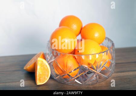 Lead crystal fruit bowl full of oranges 'fruit' against white background with cut orange wedges and copy space Stock Photo